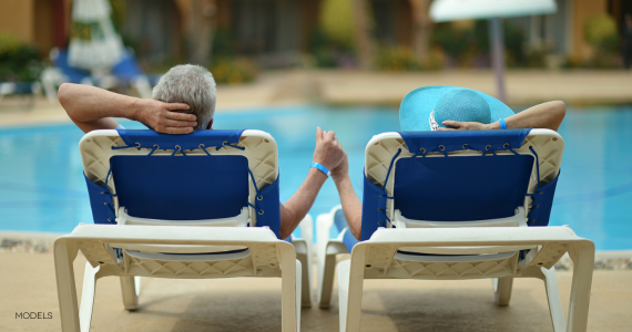 older middle aged couple sitting in chairs by pool