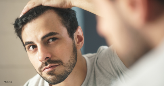 man looking in mirror and holding back top of hair to look at roots