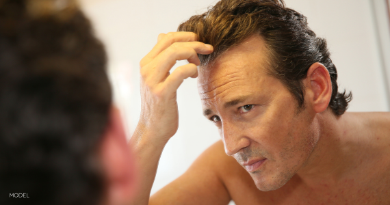 middle aged man looking at his hair in the mirror