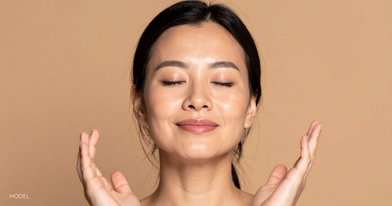woman with eyes closed, slight smile on her face, and hands framing face