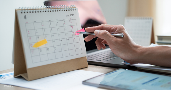 male hand pointing to calendar with pen, dates marked off with sticky flags